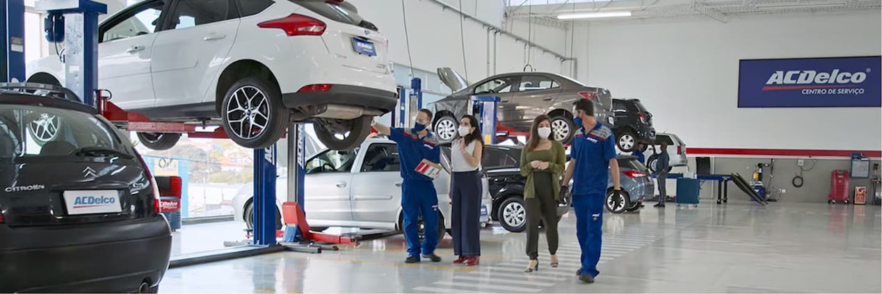 Centro automotivo, com carros para revisão e atendente mostrando o carro para cliente