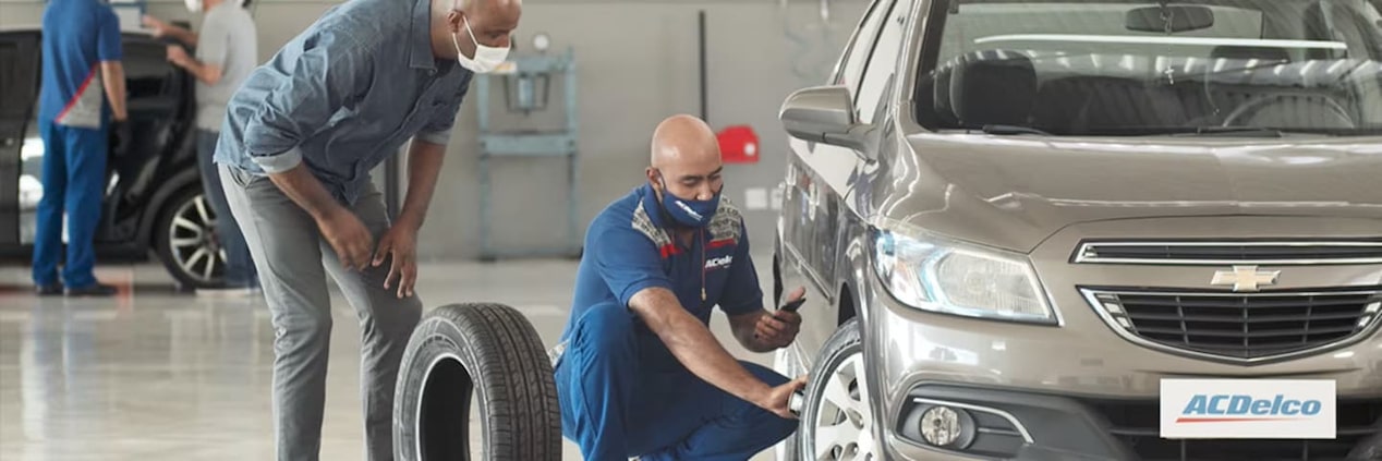 Atendente mostrando os pneus de um carro para cliente.